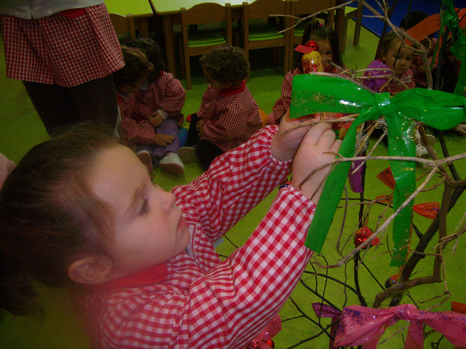 Niña decorando un árbol con lazos de colores.