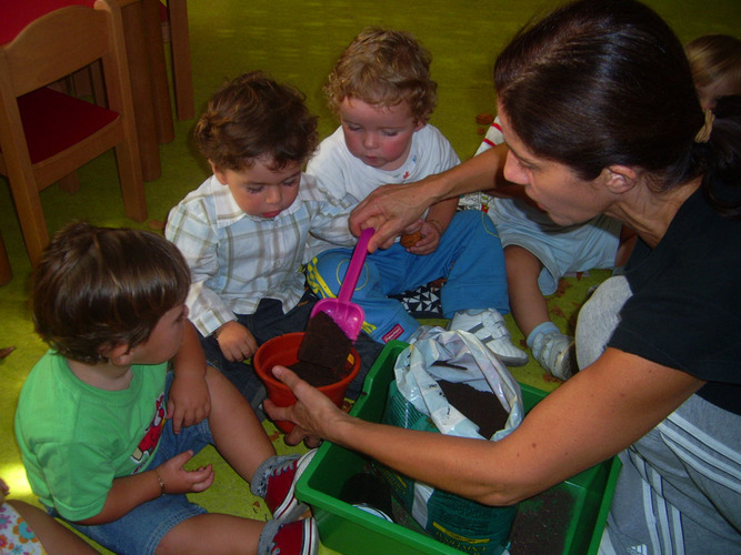 Profesora echando tierra en un tiesto junto a unos niños.