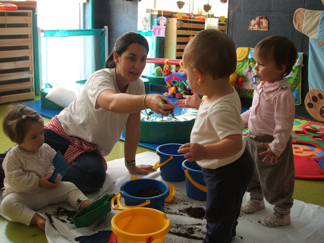 Niños pequeños junto a su profesora, jugando con tierra.