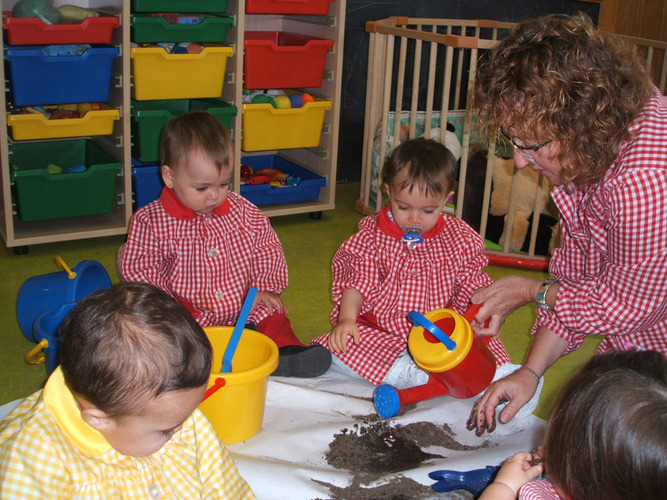 Niños pequeños junto con su profesora con una regadera, regando la tierra.