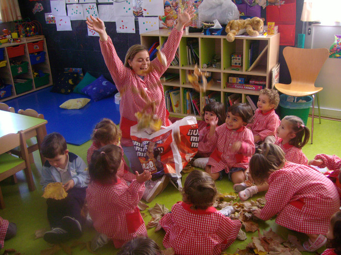 Grupo de niños y su profesora, jugando con hojas de árboles.