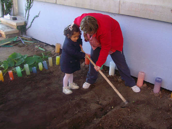 Profesora enseñando a una niña a arar un huerto.