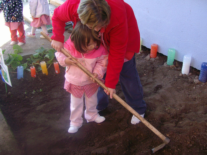 Profesora enseñando a una niña a arar un huerto.