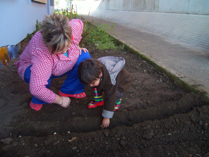 Profesora enseñando a un niño a plantar semillas en un huerto.