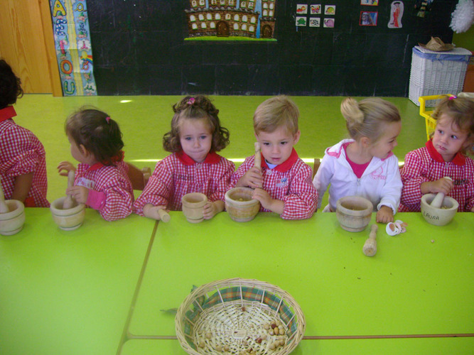 Niños machacando avellanas con unos morteros.