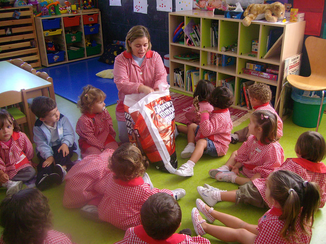 Profesora sacando hojas de arboles de una bolsa, para darsela a los niños.