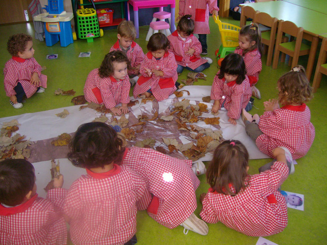 Niños decorando con hojas de árboles, un árbol pintado en un mural.