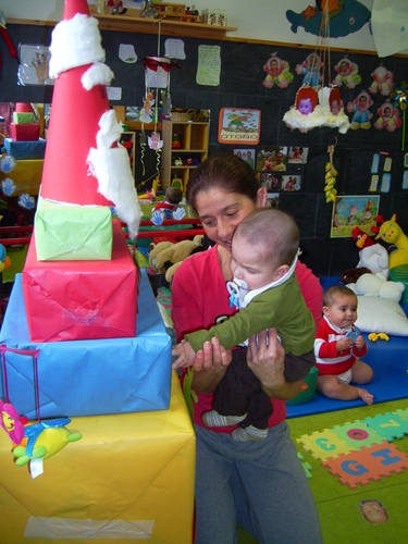 Profesora enseñandole unos regalos a un bebé con chupete.