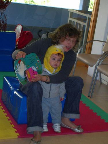 Profesora contando un cuento de una gallina, mientras un niño la acompaña disfrazado de pollito.