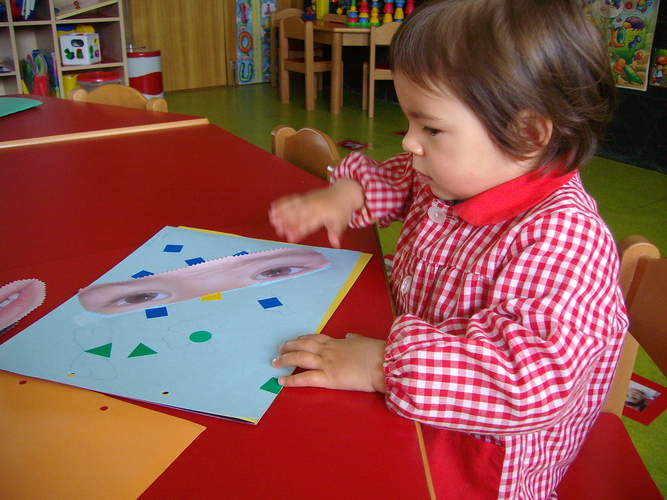 Niño pegando unos ojos recortados en una cartulina.