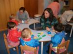 Dos madres ayudando a los niños entorno a una mesa a preparar adornos