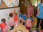 Niños pintando sobre un lienzo en la pared, observados por las educadoras