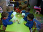 Varios niños preparando brochetas de frutas sentados entorno a una mesa