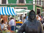 Bienvenido al mercado, estatua de vendedora con el mercado funcionando al fondo